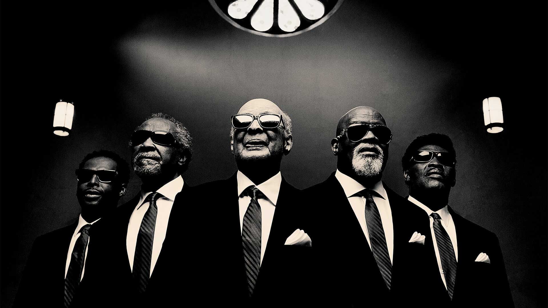 Dressed in black suits and sunglasses, five members of The Blind Boys of Alabama prepare to sing Gospel favorites.